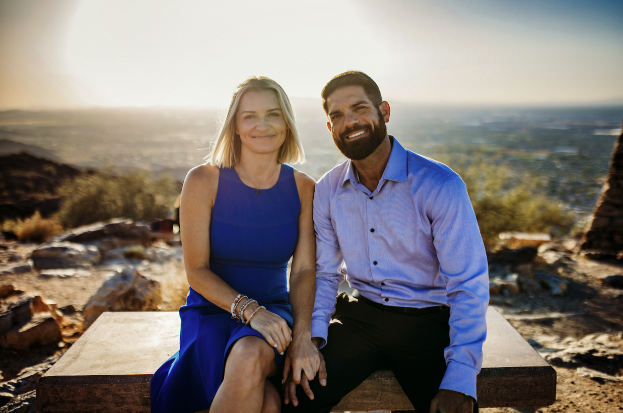 Terrah and Jon Shaw, seated together on a stone bench on a desert hillside, with the valley behind them.